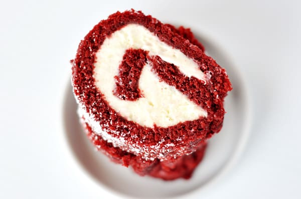 slices of a red velvet cake roll with a cream cheese filling stacked on a white plate