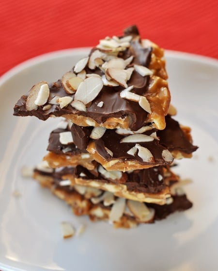 Pieces of almond roca stacked on a white plate.