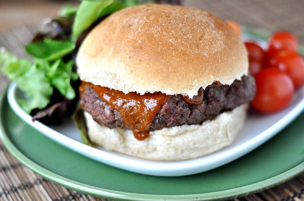 Grilled burger in a bun with some lettuce and tomatoes on the side all on a white plate.