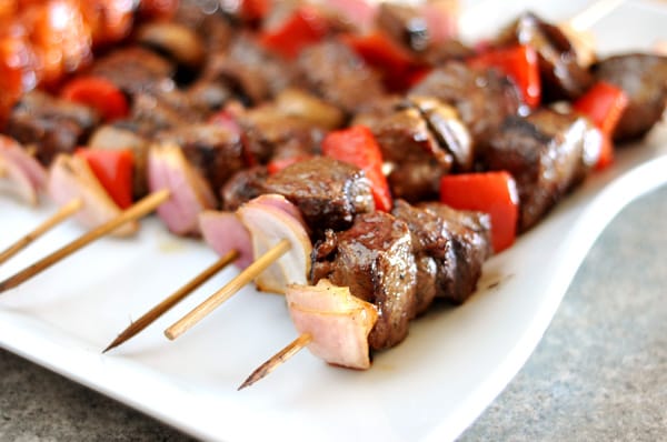 White platter full of grilled beef and vegetable kebabs. 