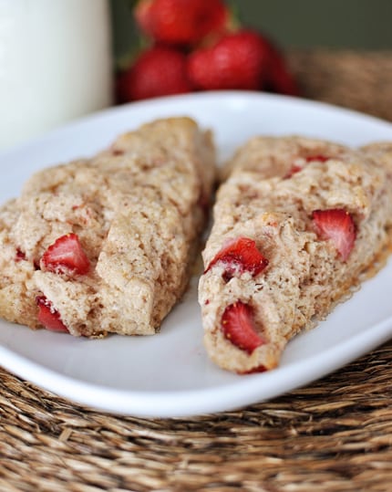 Two scones with pieces of strawberry laying next to each other on a white plate.