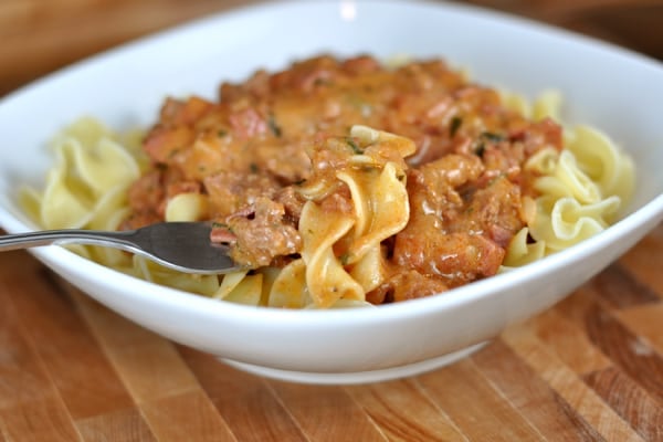 White bowl with cooked noodles topped with beef stroganoff.