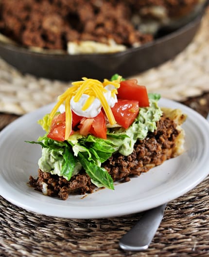 A white plate with a slice of skillet taco pie topped with lettuce, tomatoes, sour cream, and cheese.