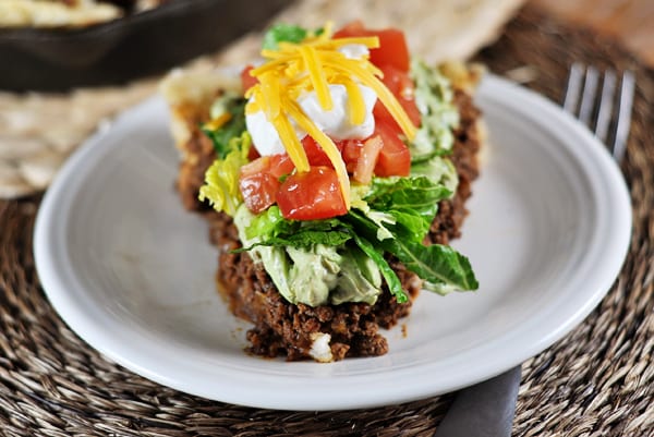 White plate with a slice of taco pie topped with lettuce, chopped tomatoes, cheese, and sour cream.