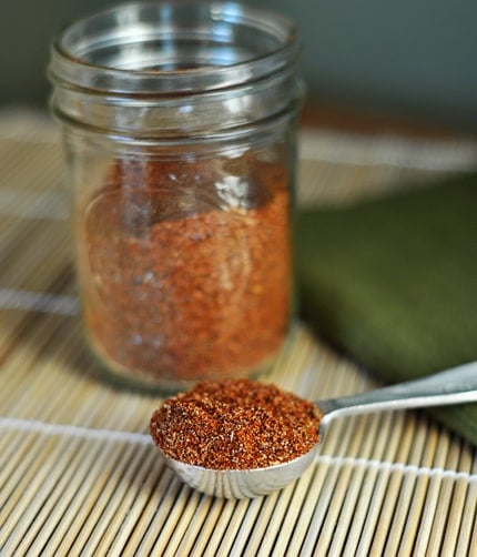 Homemade taco seasoning in a mason jar and scooped in a silver tablespoon in front of the jar.