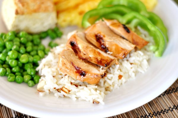 A white plate with white rice, chicken strips on top, green pepper slices, and green peas.