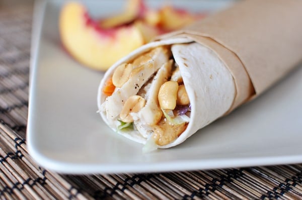 White tortilla wrap filled with asian chicken and peanut sauce, with fresh peach slices in the background.