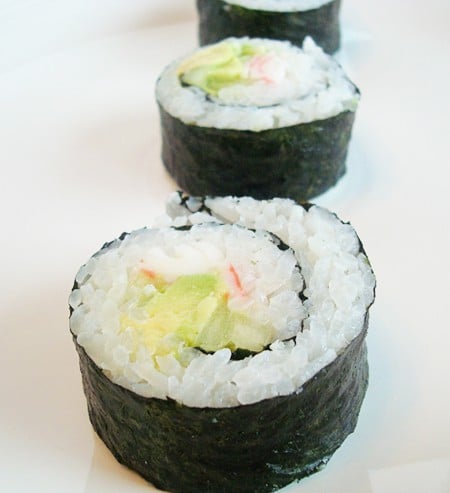 Three California sushi rolls in a row on a white plate.