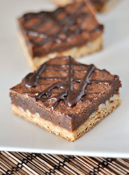 A square bar with a blondie base, brownie top, and ganache drizzle.