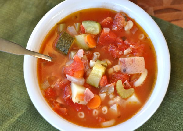 Top view of a white bowl full of minestrone soup filled with pasta and chopped vegetables.