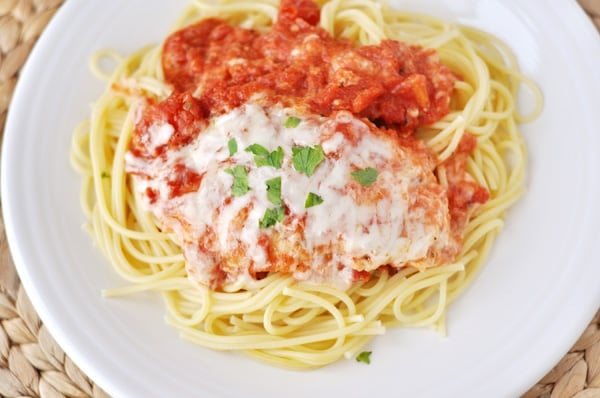Top view of chicken parmesan over a bed of noodles on a white plate.