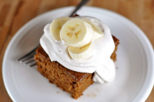 Top view of a piece of brown gingerbread cake topped with whipped cream and sliced bananas.