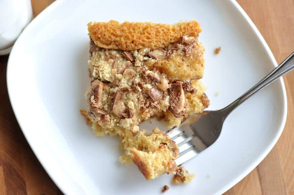 Top view of a piece of Heath Bar cake on a white plate with a bite being taken out with a fork.