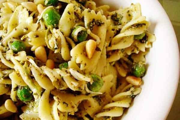 Pesto pasta with pine nuts and peas in white bowl.