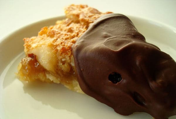 Coconut bar in triangle shape, half dipped in chocolate, on a white plate.