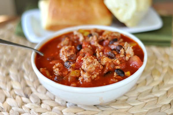 White bowl with black bean turkey chili and a plate of bread in the background.