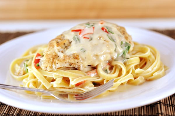 A white plate with cooked fettuccine, breaded chicken, and a pepper cream sauce.