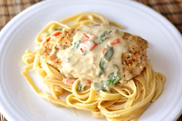 Top down view of a white plate with cooked fettuccine, a breaded chicken breast, and a pepper cream sauce.