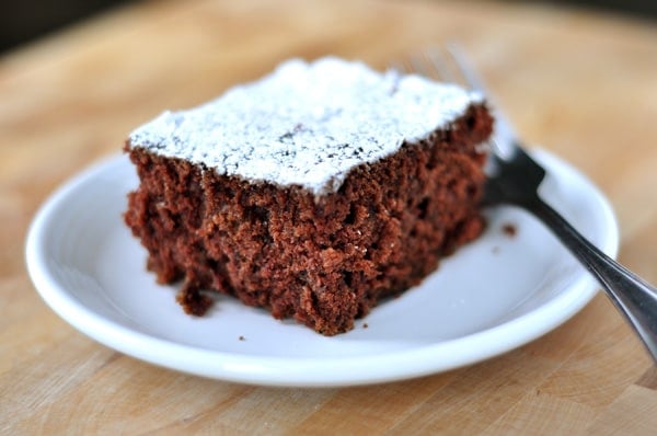 A piece of powdered sugar dusted cake on a small white plate.