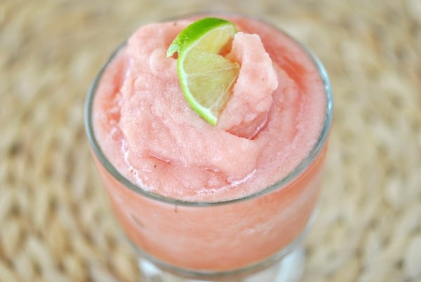 A pink watermelon smoothie topped with a slice of lime in a clear goblet.