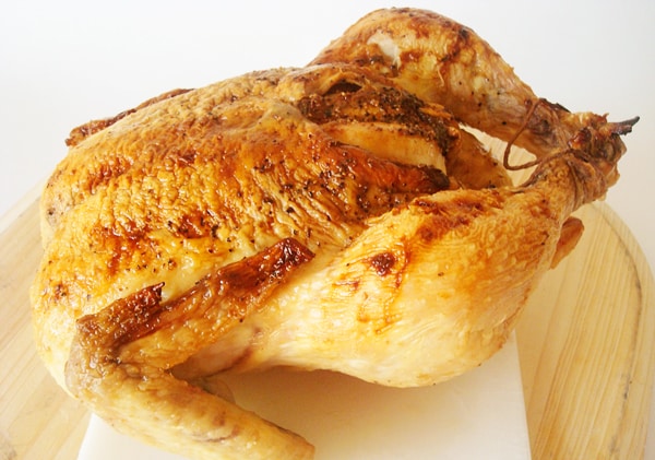 Whole roasted chicken on a white cutting board.