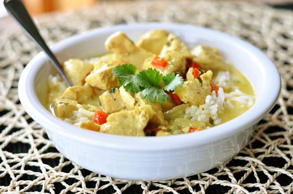 White bowl with chicken curry soup over a bed of white rice.