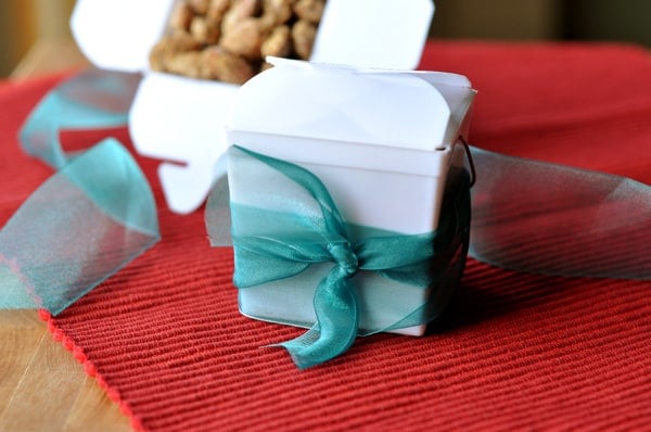 White takeout containers with blue ribbons tied around them filled with candied almonds.