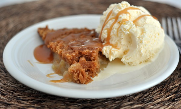 white plate with a piece of apple pie and scoop of vanilla ice cream drizzled with caramel
