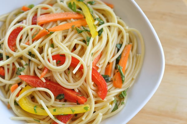 Top view of a white bowl with cooked spaghetti noodles and sliced peppers.