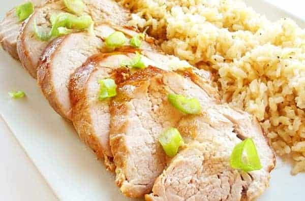 Sliced pork tenderloin and brown rice on a white platter.