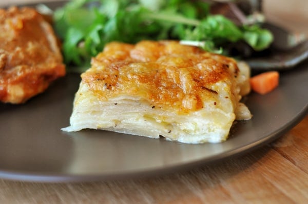 Brown plate with a serving of au gratin potatoes and lettuce on the side.