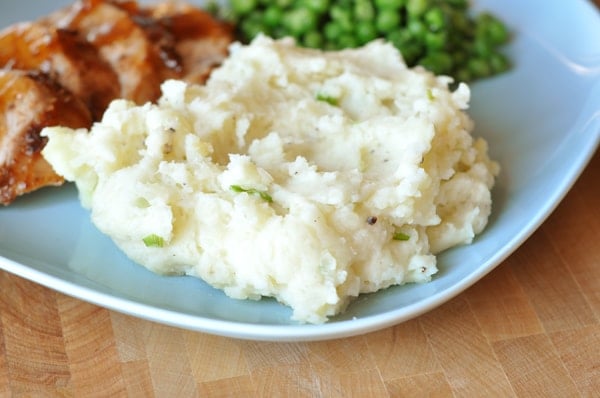 a scoop of mashed potatoes with green peas and pork on the plate behind it