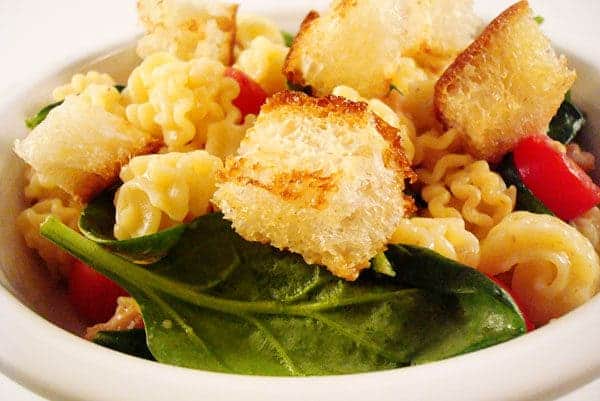 White bowl with spinach, pasta, and croutons.