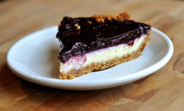 Slice of cheesecake with blueberry topping on a white plate.