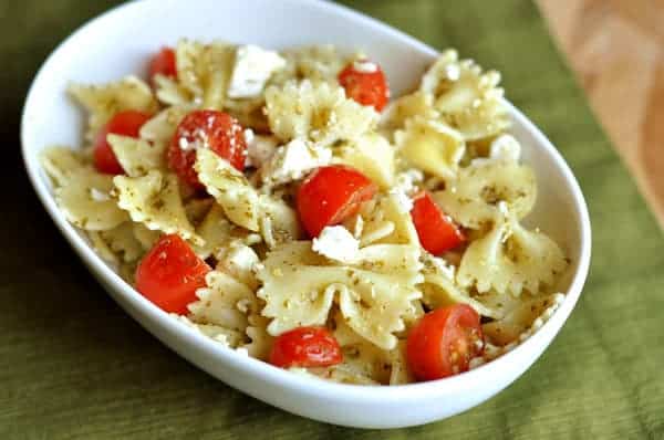 White bowl full of cooked bowtie pasta, sliced cherry tomatoes, and feta.