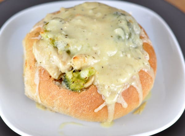 Top view of a bread bowl on a white plate with broccoli and melted cheese inside.