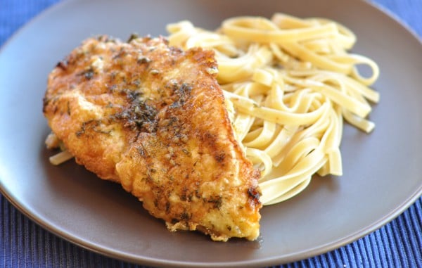 Breaded chicken and cooked pasta on a brown plate.