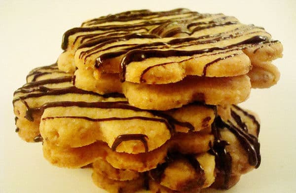 Stack of flower shaped shortbread cookies with chocolate drizzle.