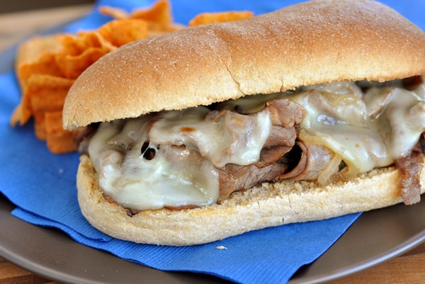 Cheesesteak sub sandwich with melted cheese sitting on a blue napkin.