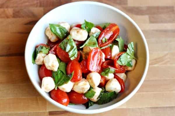 Top view of a white bowl with sliced tomatoes, mozzarella balls, and spinach drizzled in oil.