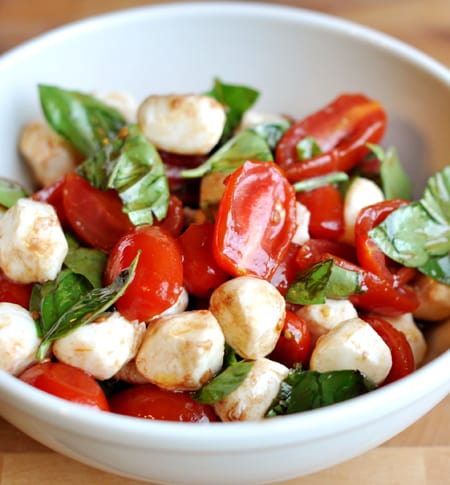 mozzarella balls, sliced cherry tomatoes, and spinach drizzled in oil in a white bowl
