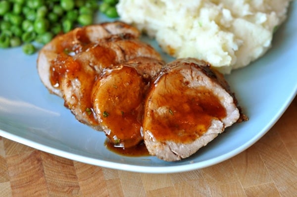 slices of pork with apricot glaze, next to mashed potatoes and peas on a blue plate