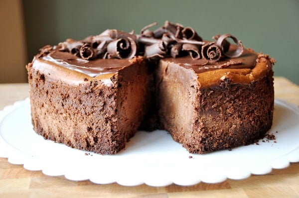 a thick chocolate cheesecake with chocolate curls on top and one slice of cheesecake cut out