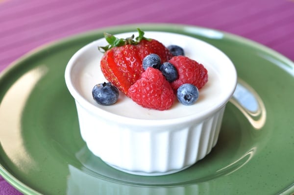 Small white ramekin filled with cream and topped with fresh berries.