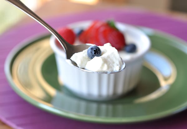 Small white ramekin with cream dessert topped with fresh berries, and a spoon taking a bite out.