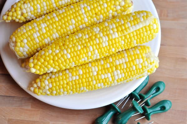 Four cooked corn on the cobs on a white plate.