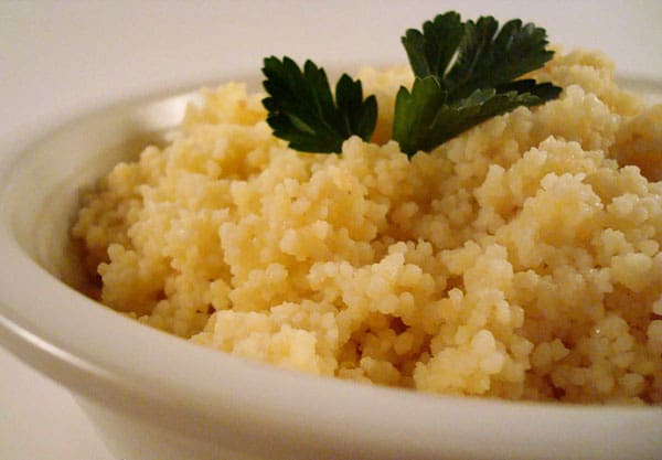 White bowl of cooked couscous with a sprig of parsley on top.