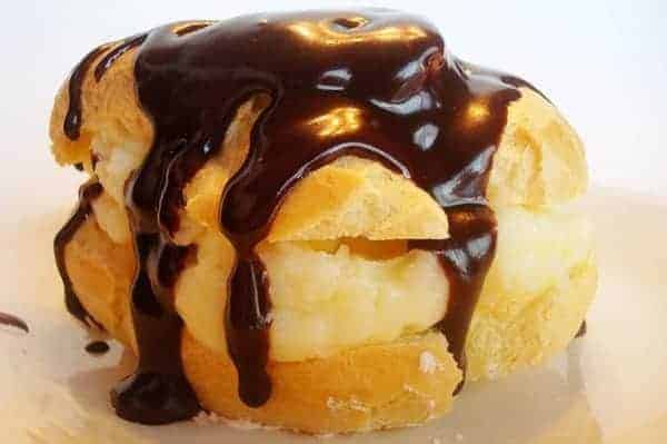 Cream puff drizzled in chocolate on a white plate.