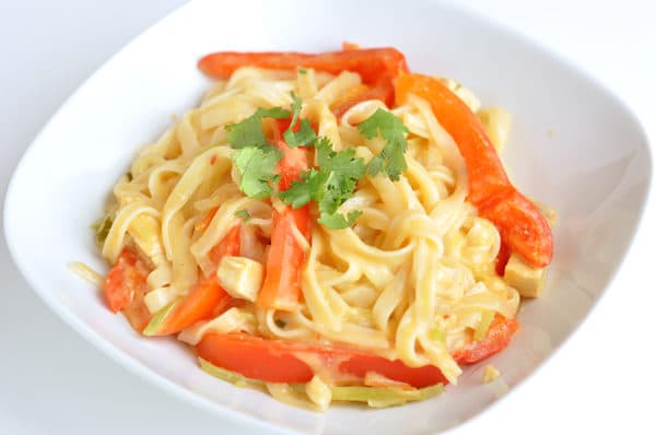 White bowl with cooked pasta and strips of red bell pepper.
