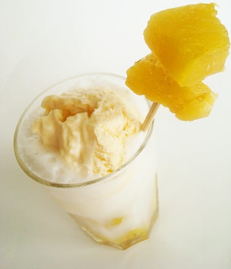 Top view of an ice cream float with a toothpick with pineapple chunks on it.